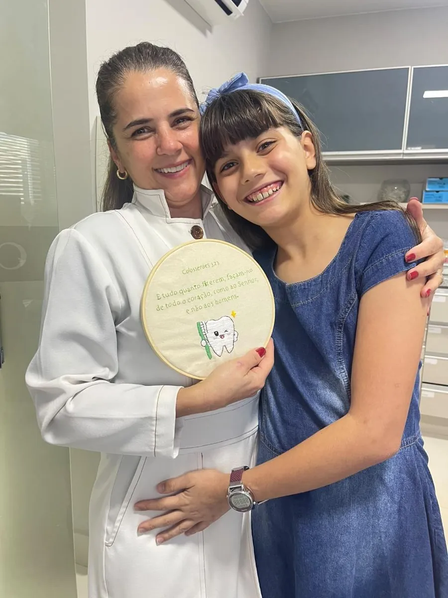 Dra. Janaína Nunes abraçada a uma paciente sorrindo no consultório